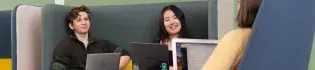 Two students at laptops smiling.