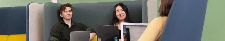 Two students at laptops smiling.