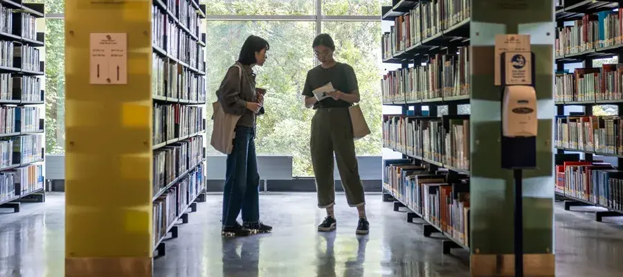 Students standing between bookshelves at the library.