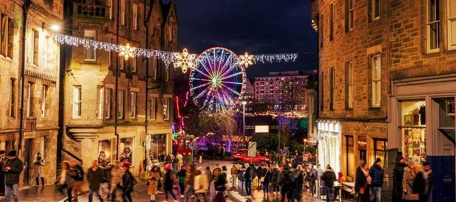 People out at night during the festive season in Edinburgh with a lit-up ferris wheel in the background.