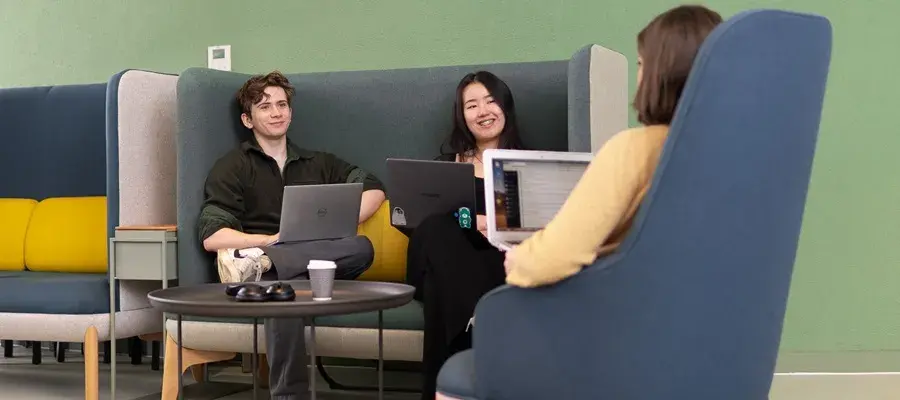 Students sitting on a sofa with laptops.