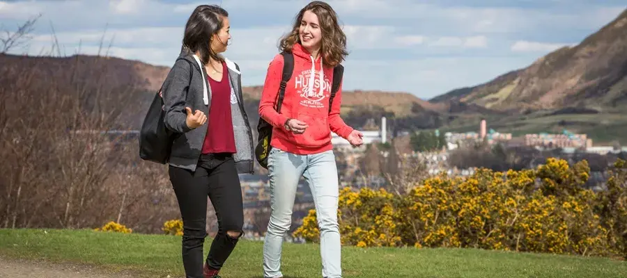 Two female students walking in Edinburgh with the city and Arthur's Seat in distance behind them.