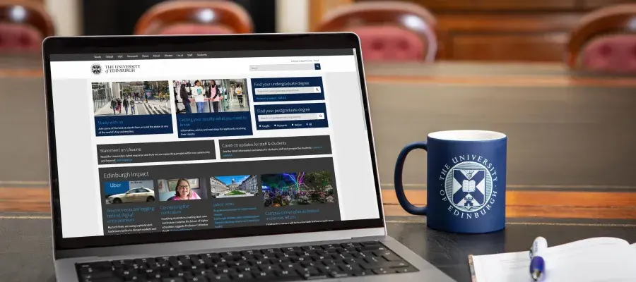 Laptop with browser window open to University of Edinburgh website, next to University of Edinburgh mug and notebook and pen.
