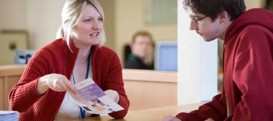 University staff holding pamphlet and talking to student at table