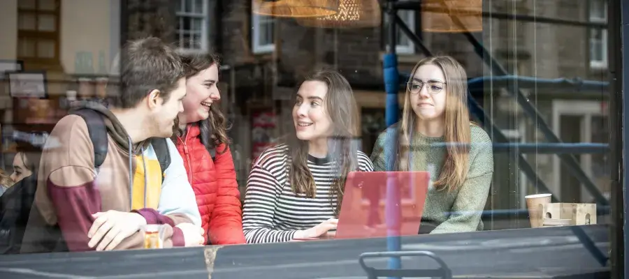 Four students sitting in a cafe with a laptop and talking.