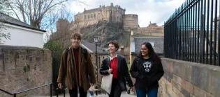 Three students walking up outdoor stairs with Edinburgh Castle behind them.