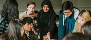 A group of international students huddled together and looking at something on a table.