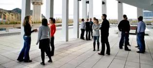 A group of students standing outside under a sheltered area with white pillars around them.