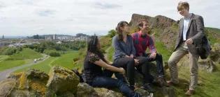 Four students atop Arthur's Seat with a view of the Crags and city skyline behind them.