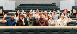 Students sitting in a lecture theatre and waving