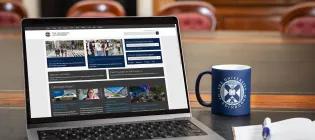 Laptop with browser window open to University of Edinburgh website, next to University of Edinburgh mug and notebook and pen.