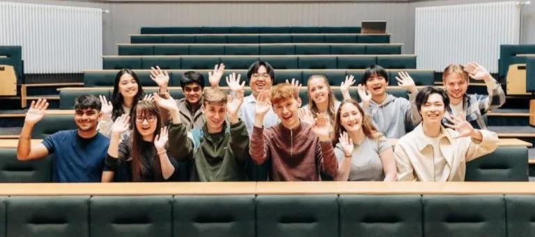 Students sitting in a lecture theatre and waving