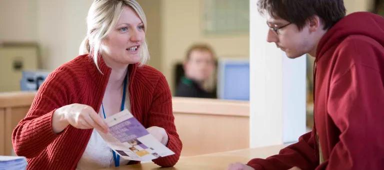 University staff holding pamphlet and talking to student at table
