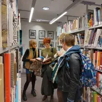 A group of people look at a book in the ECA library. They are surrounded by shelves filled with colourful books.