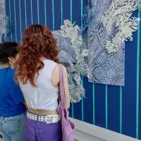 Two people are looking at an art work that fills an entire wall and is coloured in a bright blue.