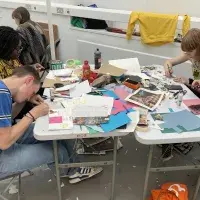A group of people sit around a table full of paper, glues, and other art materials.