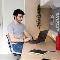 A student works on a laptop at his desk in his university accommodation.