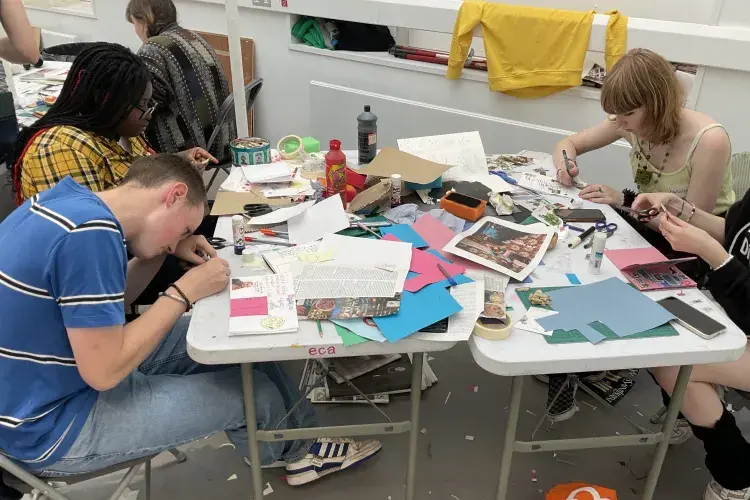 A group of people sit around a table full of paper, glues, and other art materials.