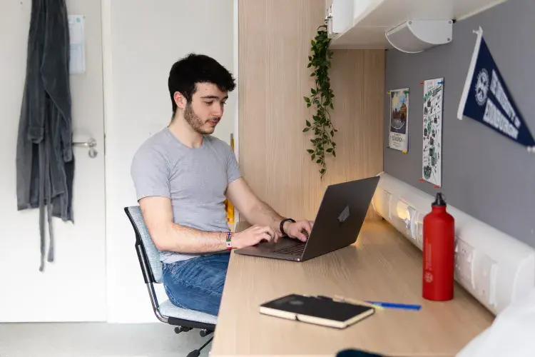 A student works on a laptop at his desk in his university accommodation.