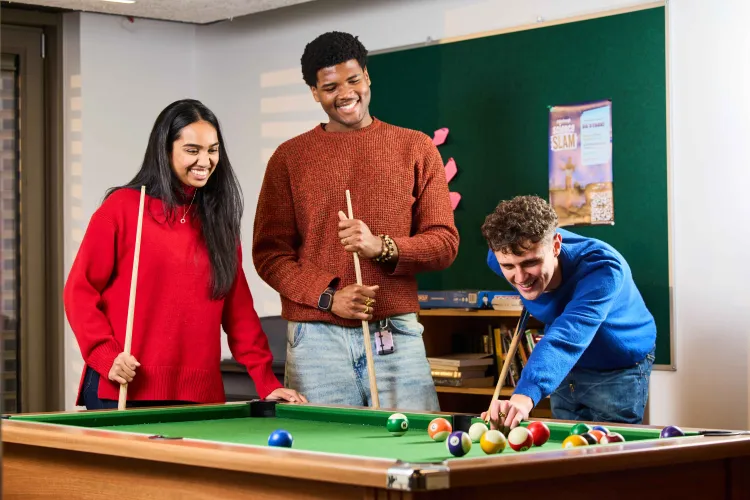 A photo of three students smiling while playing pool at Buccleuch Place Lane common room