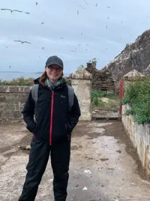 Amy poses for a photo at Bass Rock, with birds flying in the background