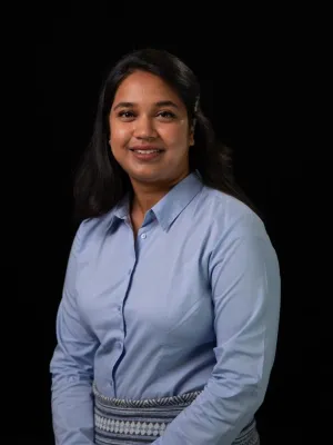 Headshot photograph featuring Ananya facing the camera, wearing a blue shirt against a black background.