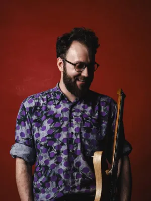 Headshoot of man holding instrument against a red background