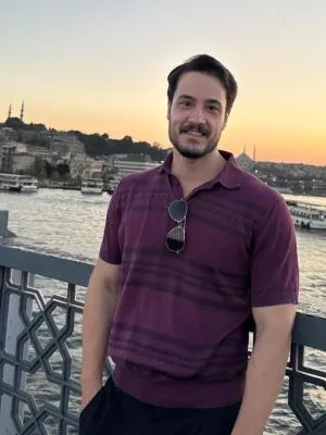 Headshot style photograph of man in purple striped t-shirt in front on a river